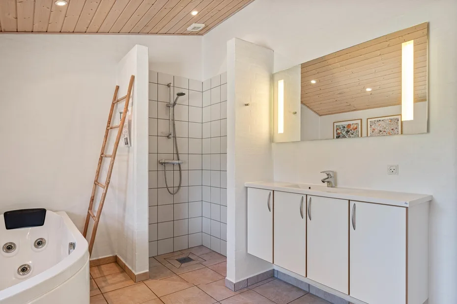 Un baño luminoso con ducha de azulejos, tocador y bañera esquinera.