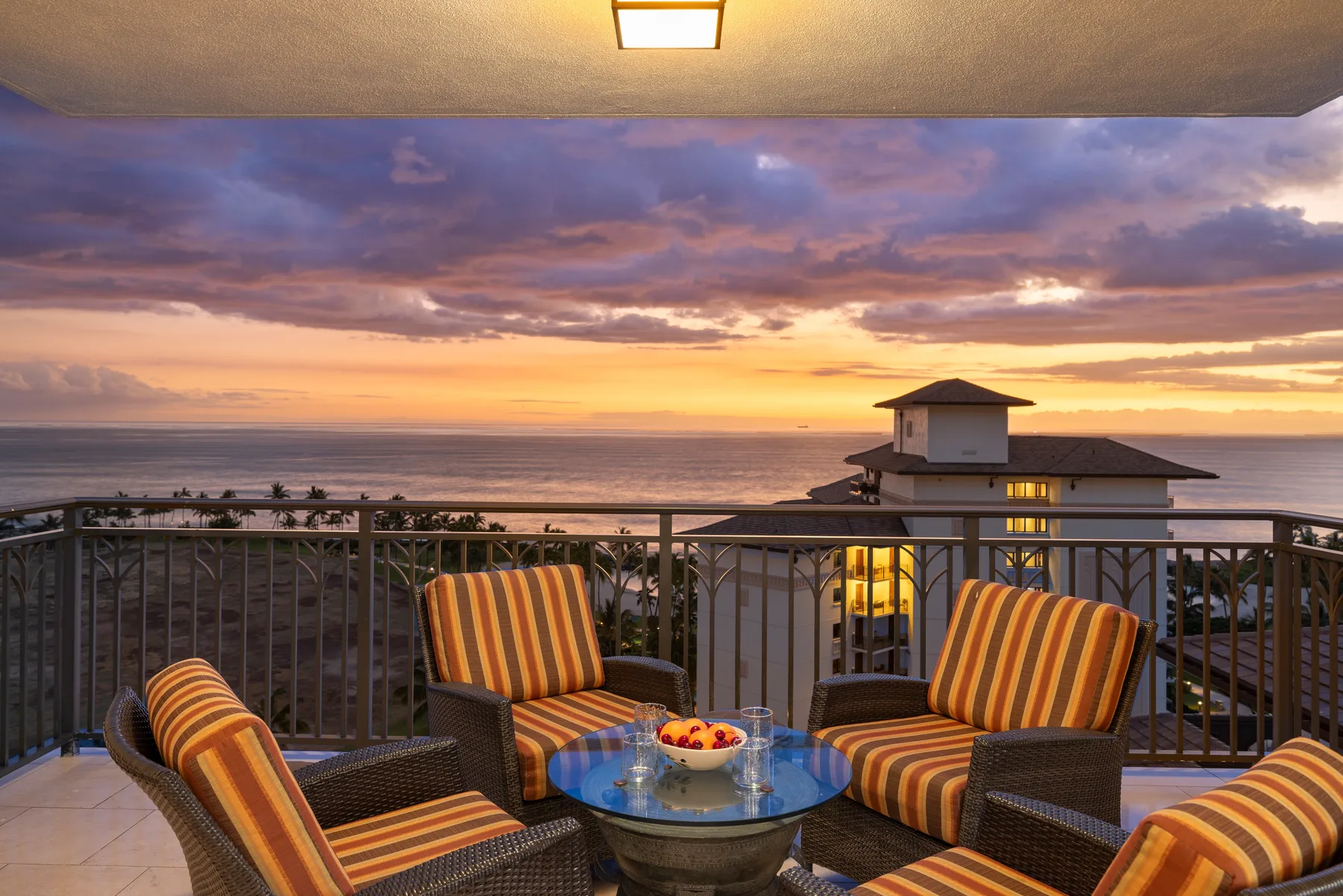 A balcony seating area overlooks the ocean at sunset.