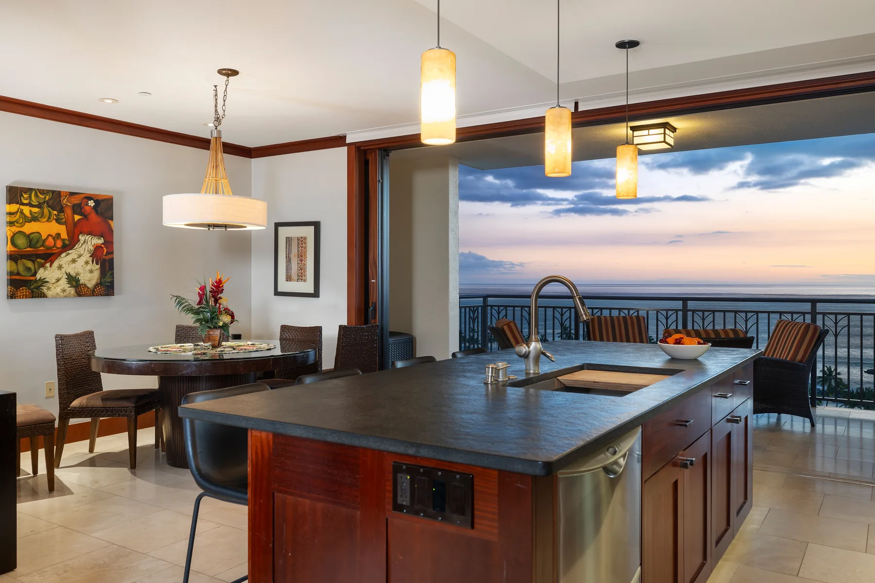 A kitchen and dining area open onto a balcony overlooking the water at sunset.