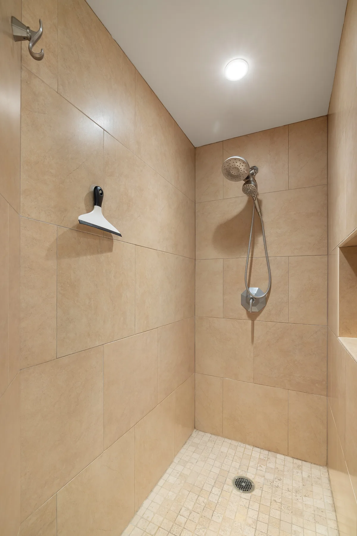 A tiled shower area with a wall-mounted showerhead and handheld sprayer.