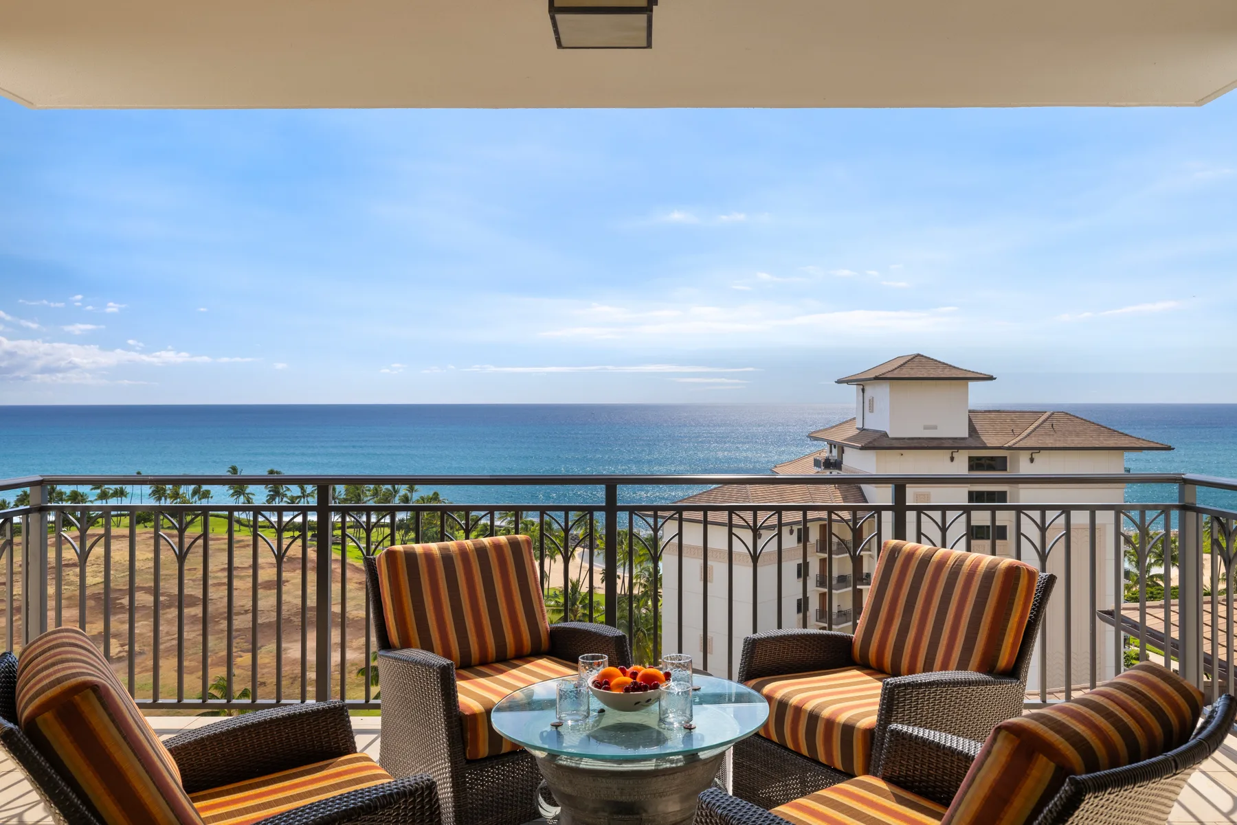 A balcony seating area overlooks the ocean, with a glass-topped table in front.