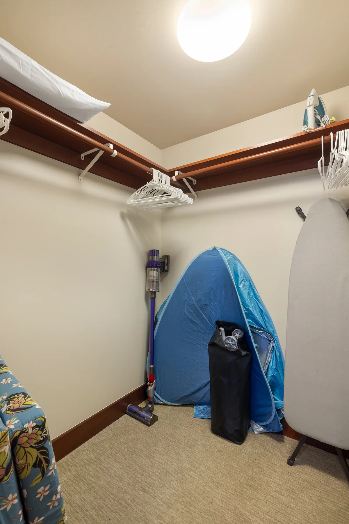 A walk-in closet with hanging rails, a vacuum, and stored items.