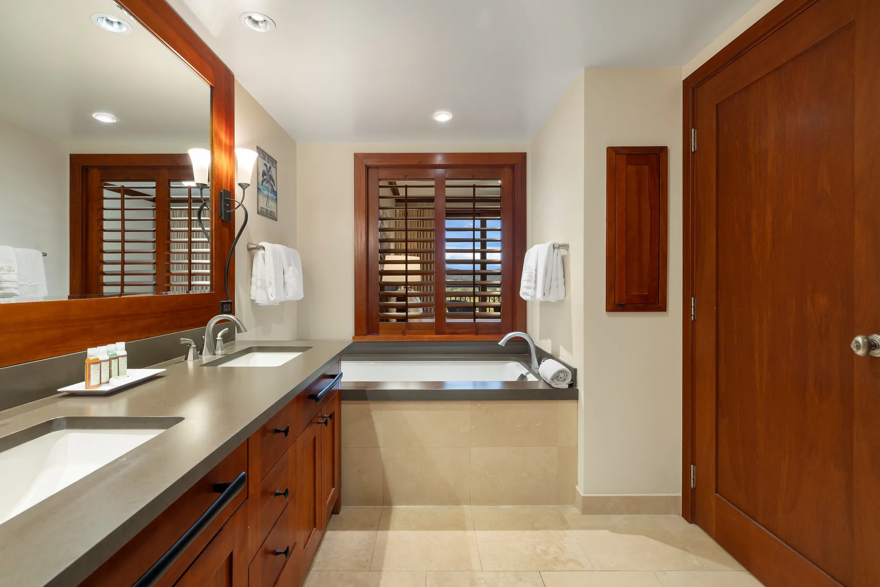 A bathroom with a long vanity, sinks, and a window with wooden shutters.