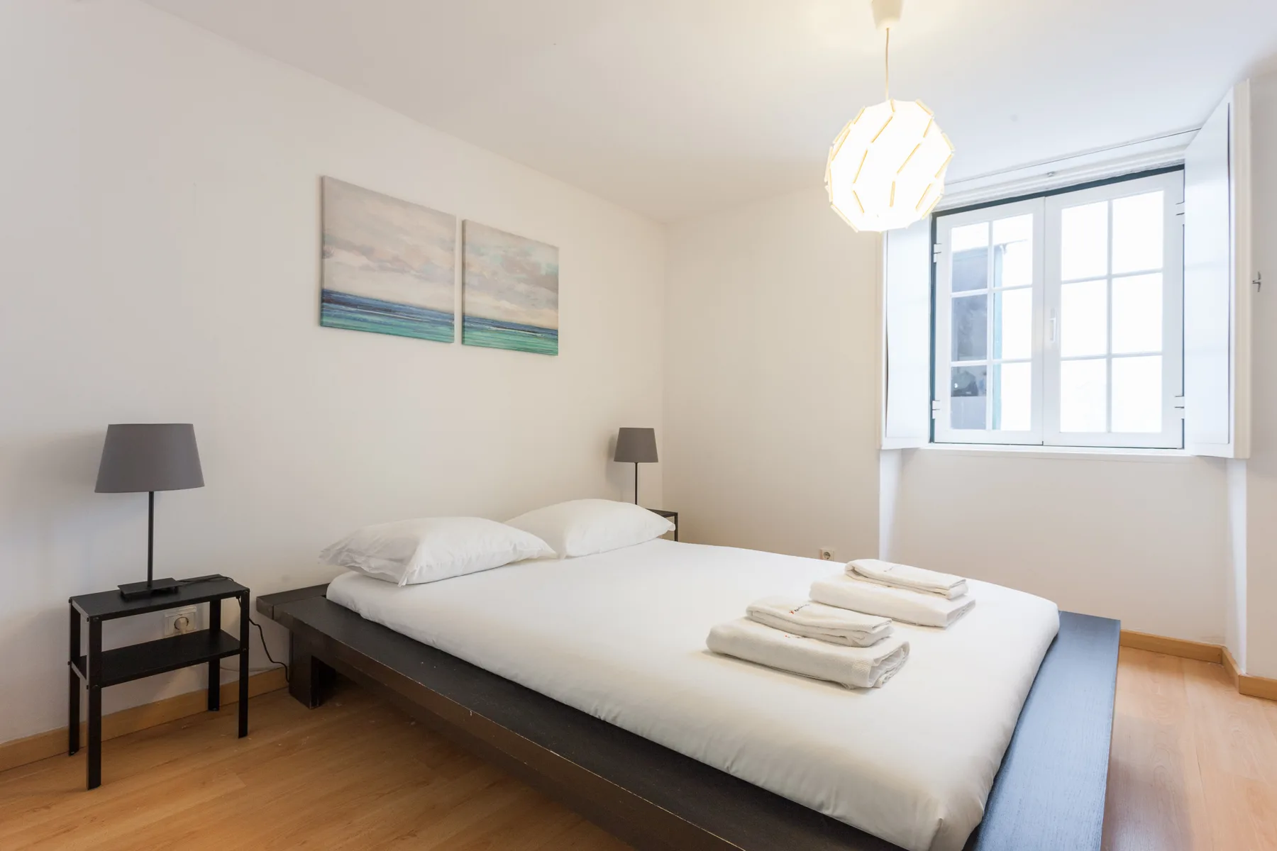 Un dormitorio luminoso con una cama bien arreglada bajo dos cuadros.