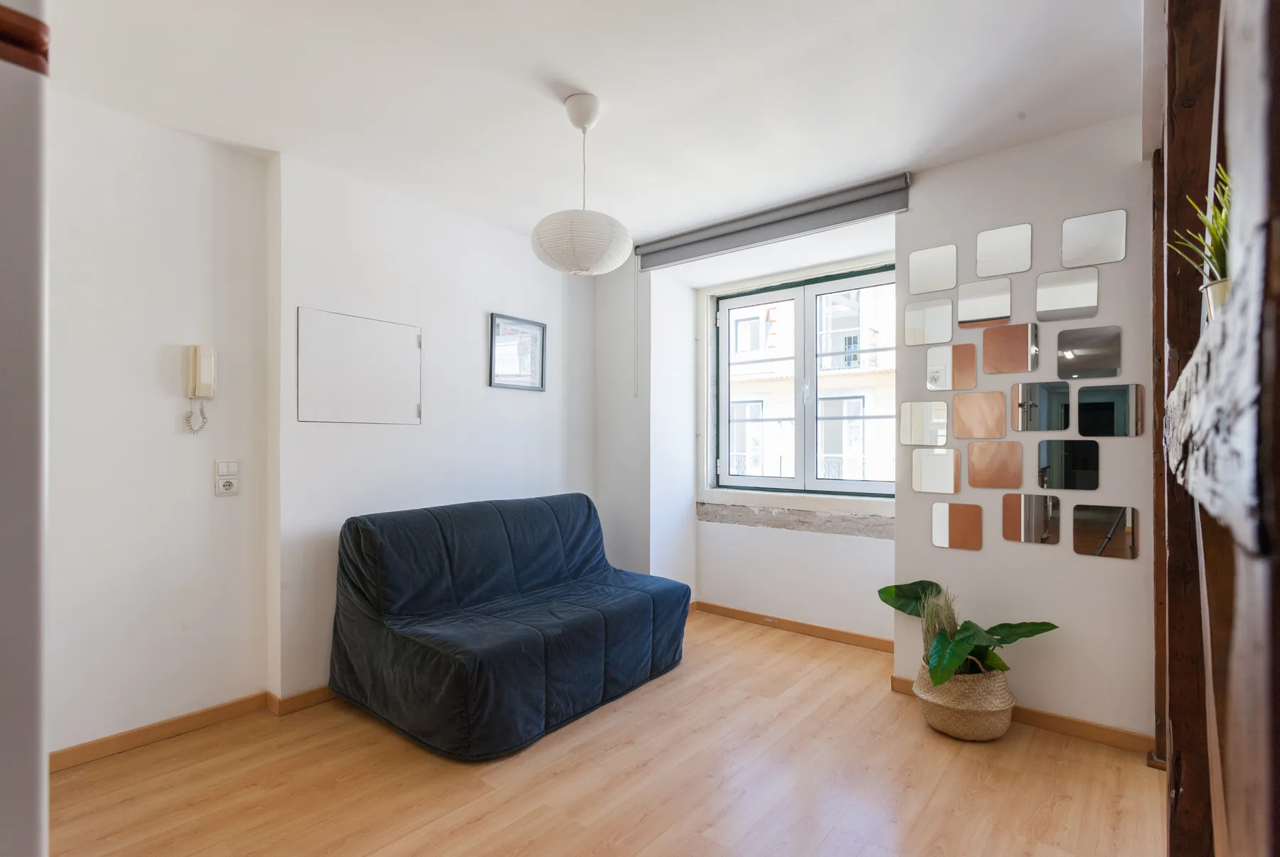 Una sala de estar luminosa con asientos azules, una ventana amplia y una planta en maceta.