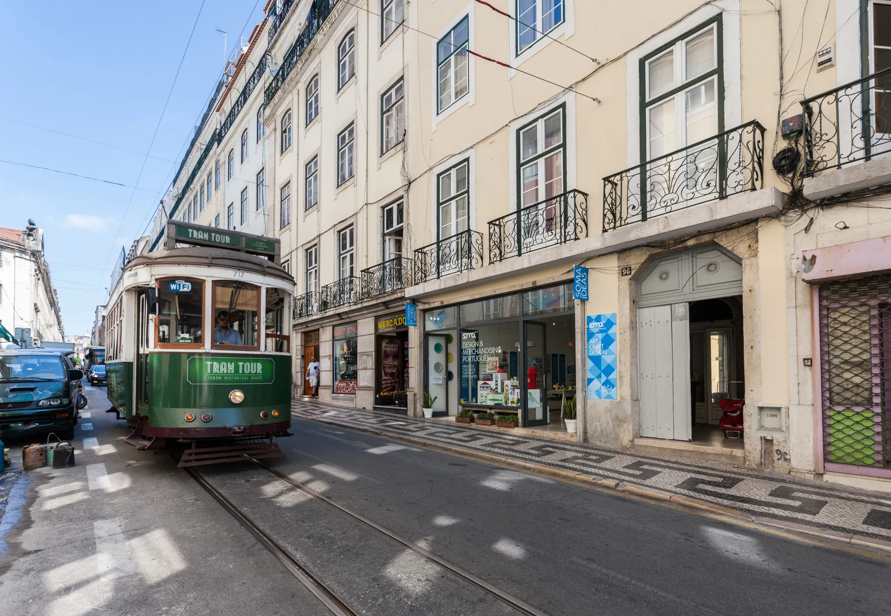 Una calle urbana con un tranvía pasando frente a comercios y edificios altos.