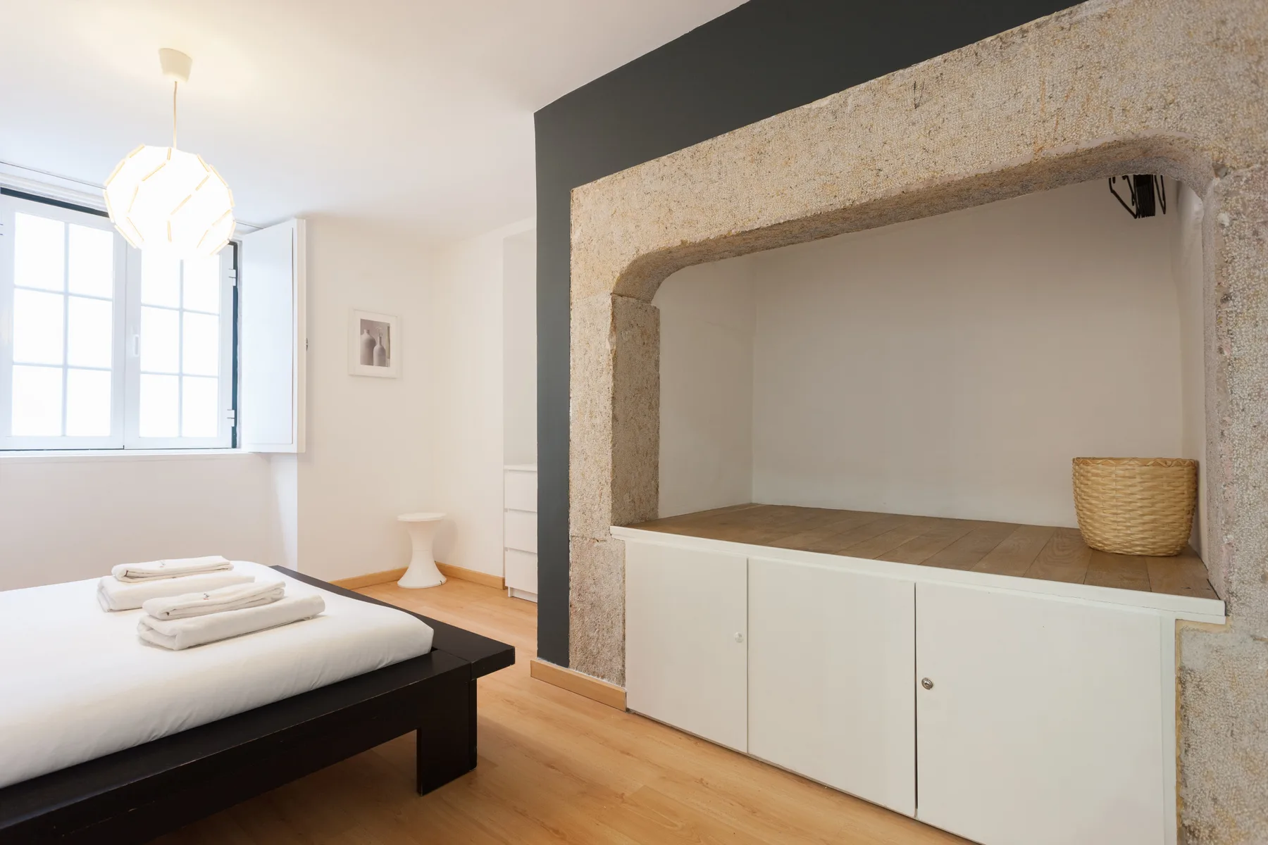 Un dormitorio con una cama junto a un armario empotrado y un amplio nicho enmarcado en piedra.