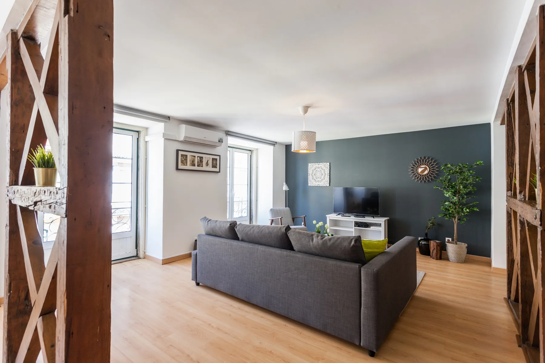 Una sala de estar con asientos grises, un televisor y ventanas altas.