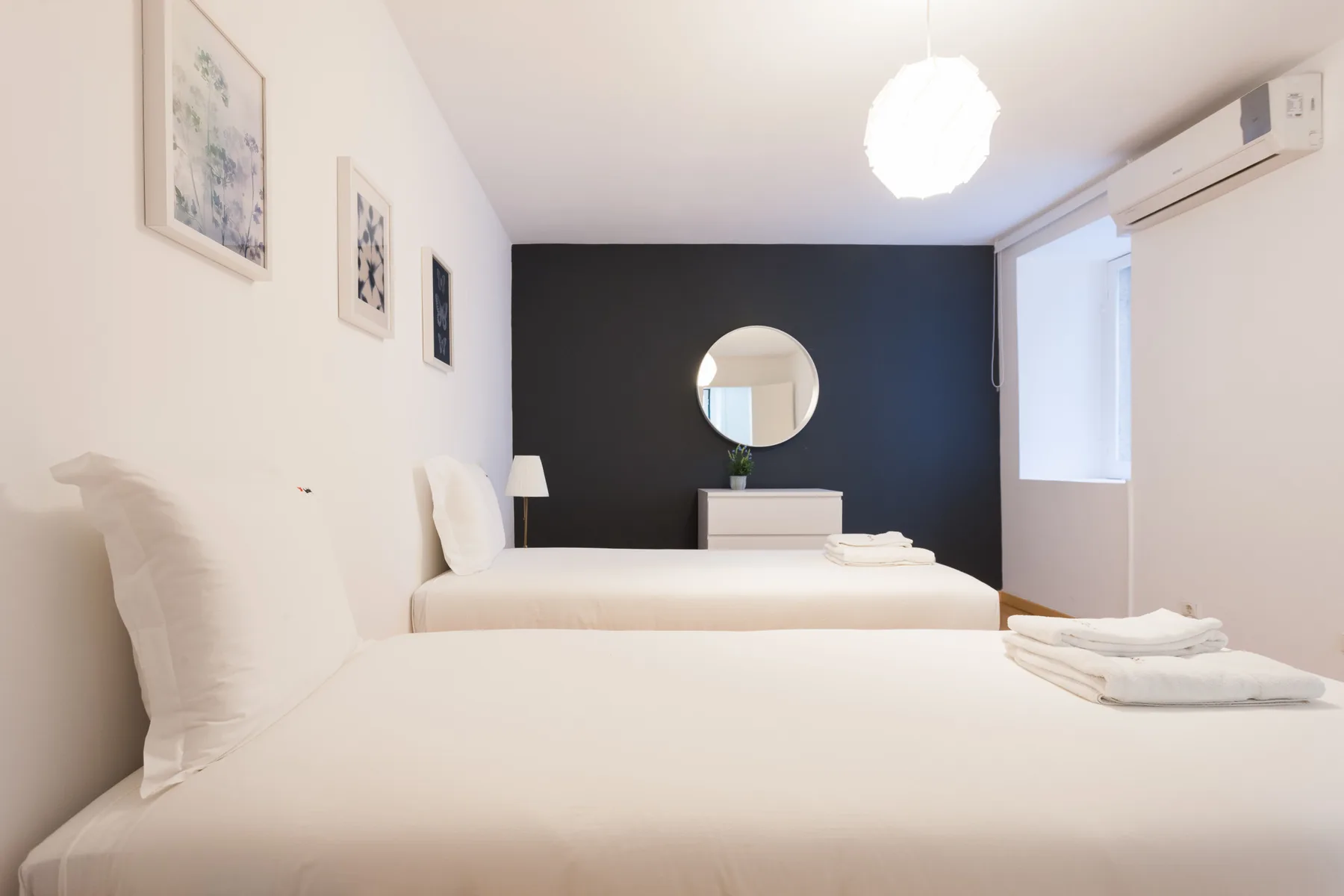 Un dormitorio con ropa de cama blanca, una pared oscura y un espejo redondo.