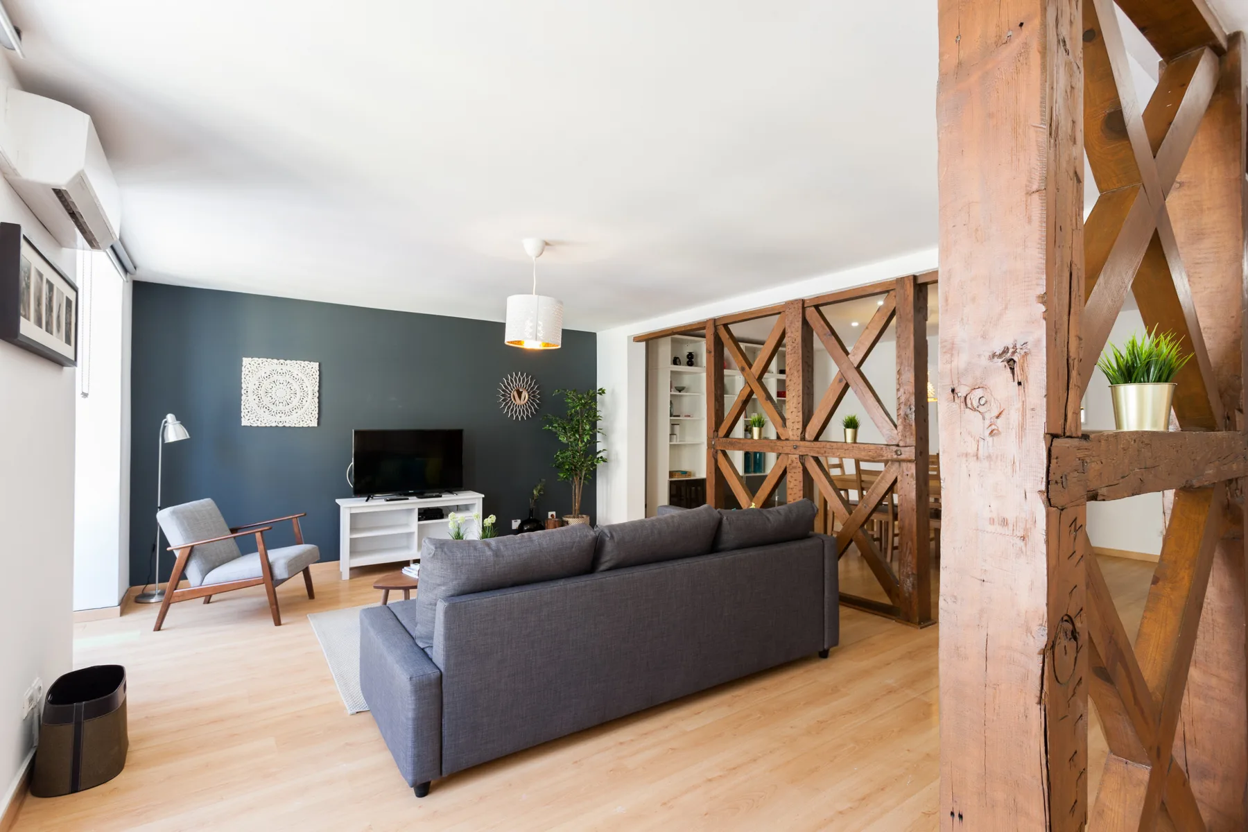Una sala de estar con asientos grises, un televisor y divisiones de madera con cruces.