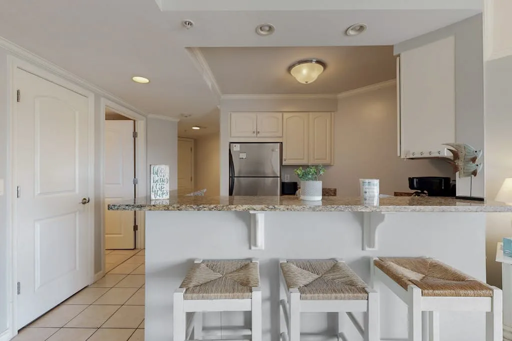 A kitchen with a breakfast counter and stools, cabinets, and a refrigerator.