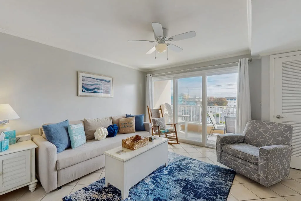 A bright living room with seating arranged around a coffee table beside large windows.