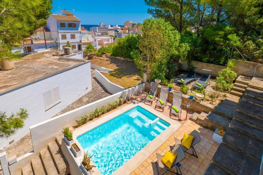 A sunlit outdoor pool is surrounded by tiled seating areas and greenery.