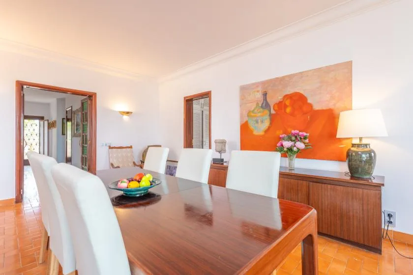 A dining room with a long table, white seating, and colorful wall art.