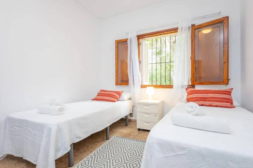 A bright bedroom with two beds and a window dressed with sheer curtains.