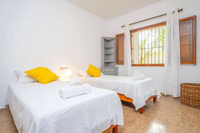 A bedroom with two beds dressed in white and a window with curtains.