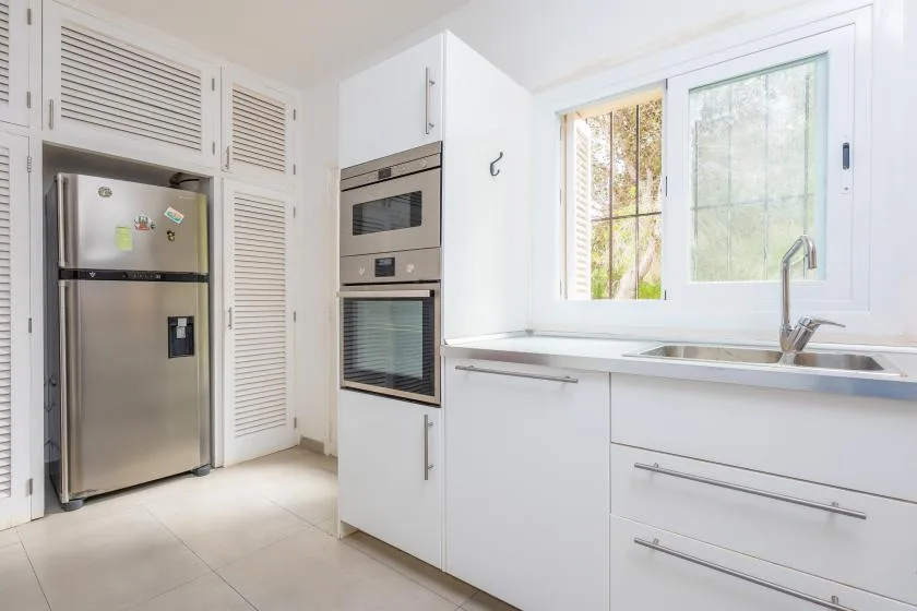 A bright kitchen with white cabinets, a refrigerator, and a sink beneath a window.