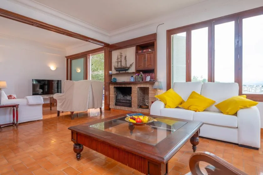 A living room with white seating, a fireplace, and large windows.