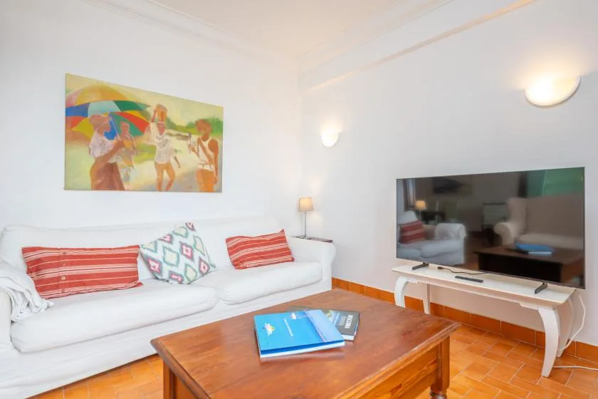 A bright living room with white seating, colorful artwork, and a wooden coffee table.