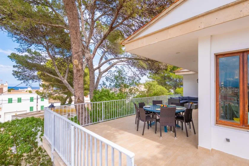 An outdoor terrace with a dining table and seating beside a white building.