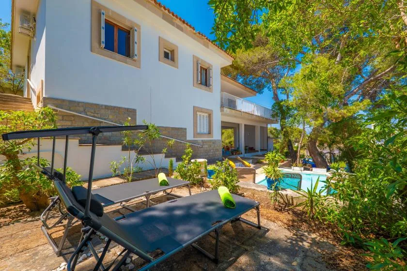 A house and outdoor patio with seating beside a swimming pool and trees.