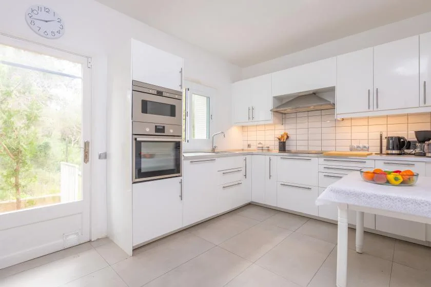 A bright white kitchen with built-in appliances and a small table.