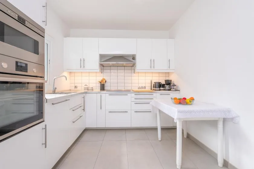 A bright white kitchen with built-in appliances and a small dining table.