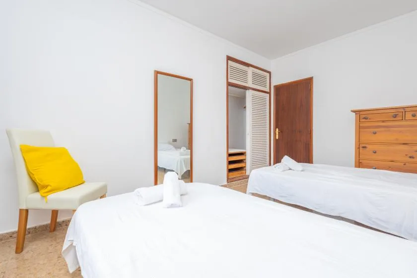 A bright bedroom with two beds, a yellow cushion, and a wooden dresser.