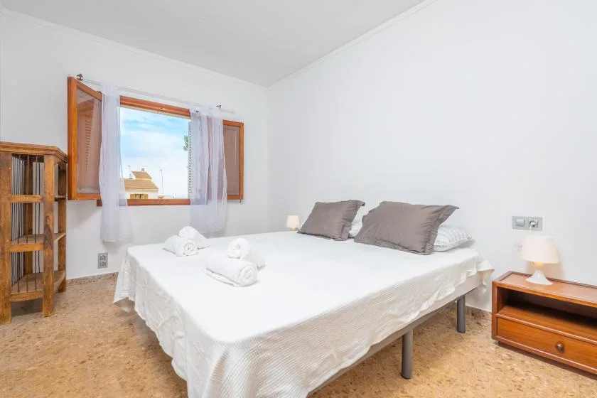 A bright bedroom with a neatly made bed beside an open window.