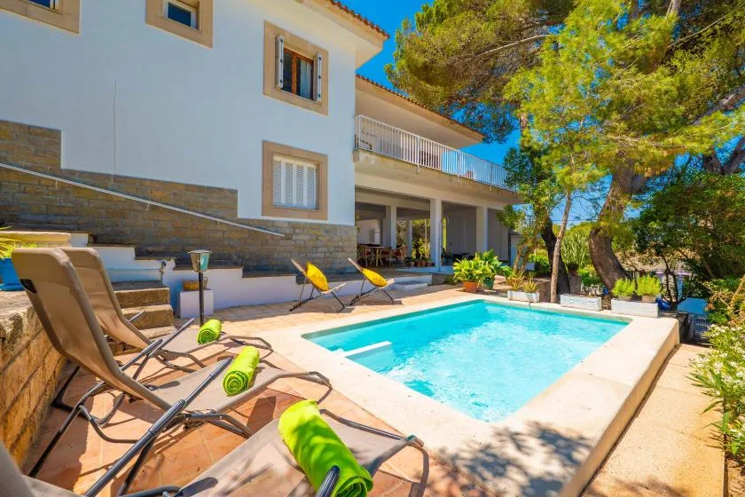 An outdoor swimming pool beside a house, with lounge chairs on the surrounding patio.