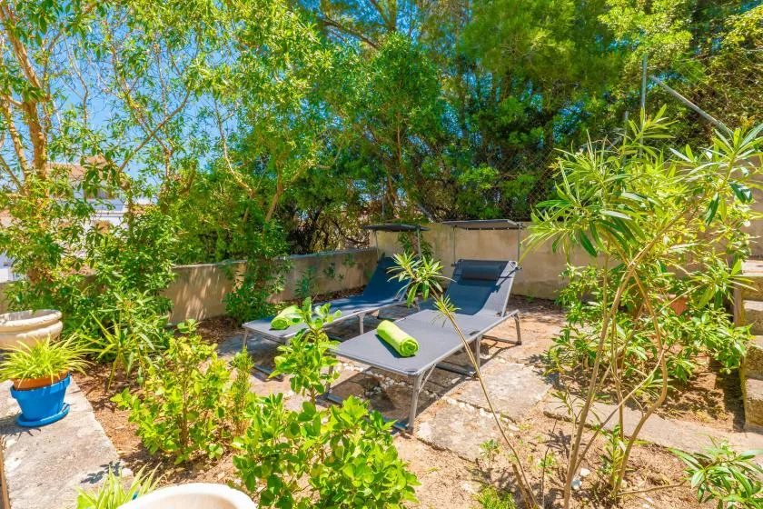 An outdoor patio has two lounge chairs surrounded by leafy plants.