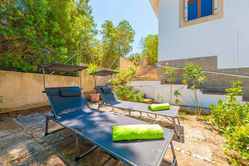 An outdoor patio has reclining loungers with bright green cushions beside a white building.