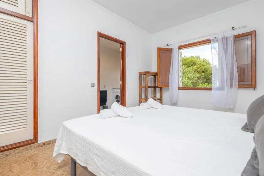 A bedroom with a neatly made bed beside an open window.