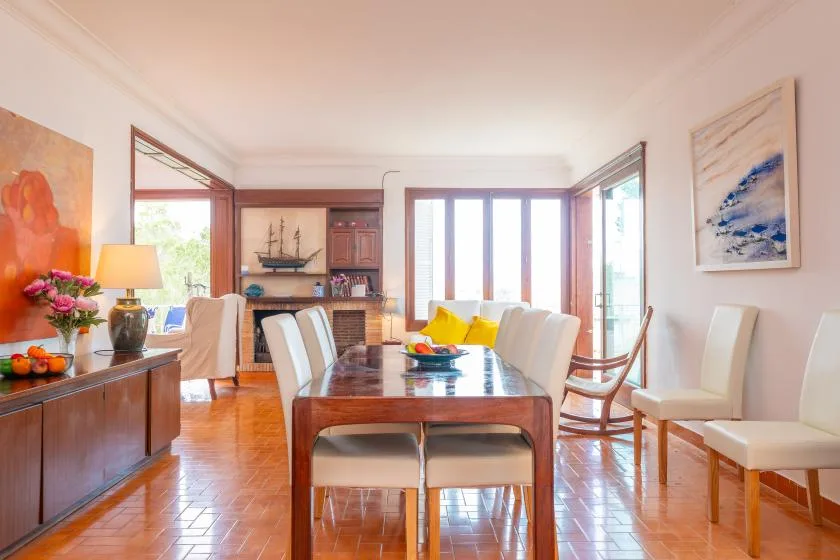 A bright dining area with a long wooden table and chairs beside large windows.