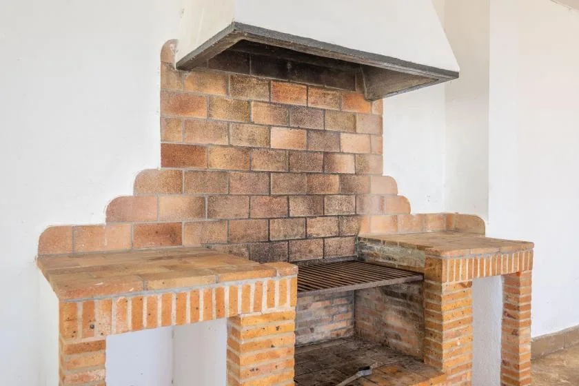 A brick fireplace with a metal grate sits beneath a white hood.