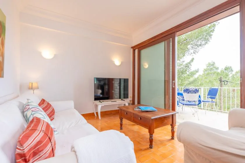A bright living room with seating, a television, and an open sliding door to a balcony.