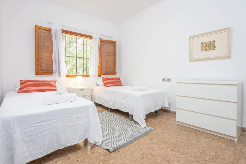 A bright bedroom with two single beds and a window with wooden shutters.