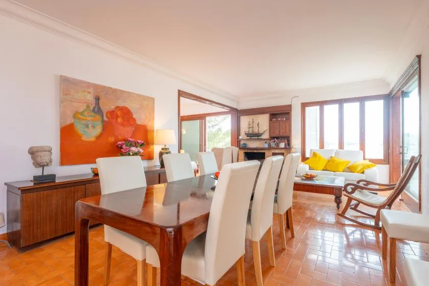 A dining and living area with a wooden dining table and bright windows.