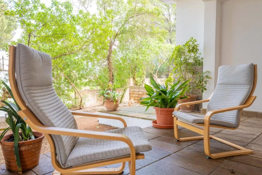 A covered patio with cushioned seating and potted plants overlooks a leafy garden.