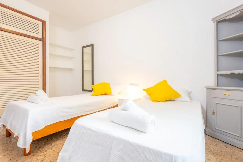 A bright bedroom has two beds with white linens and yellow pillows.