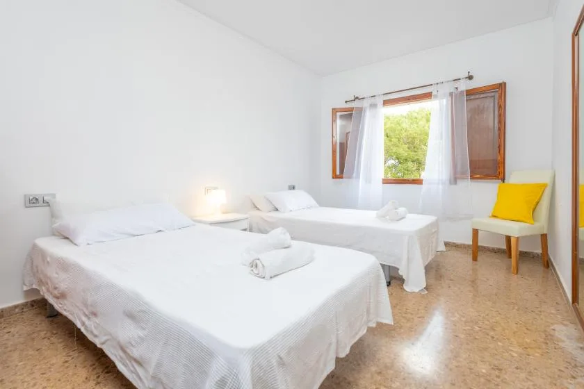 A bright bedroom with two beds and a window with open wooden shutters.