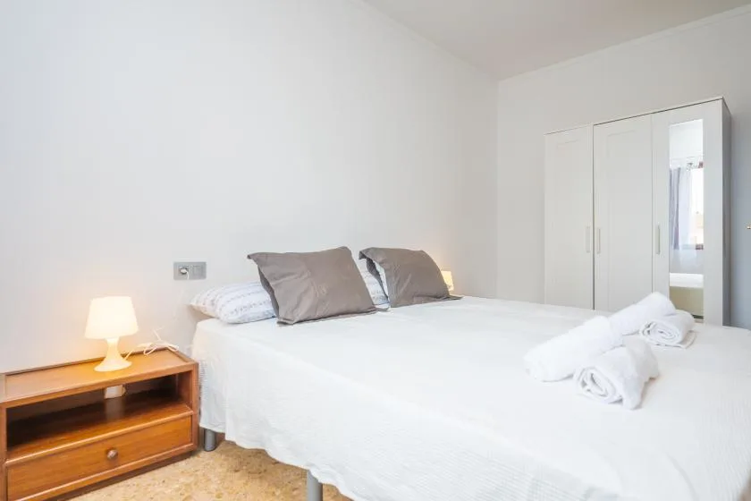 A bedroom with a neatly made bed and a wooden bedside table.