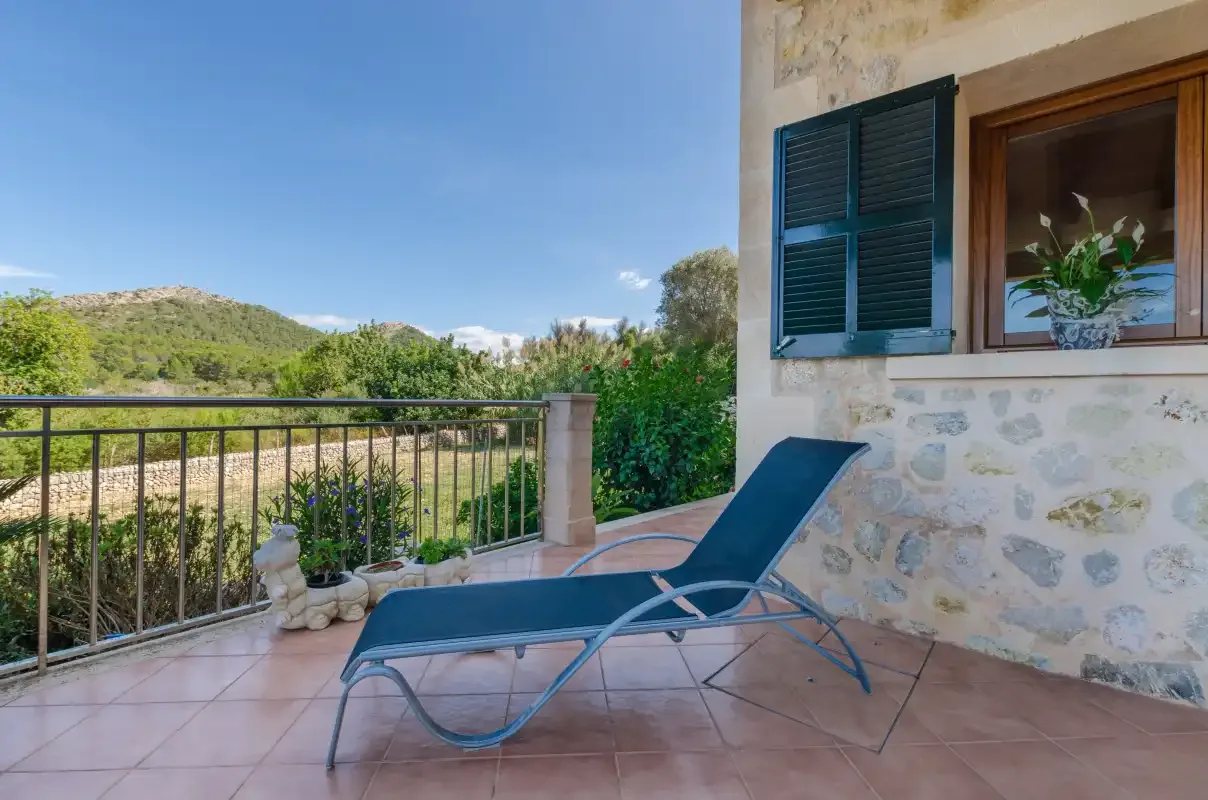 A tiled terrace with a blue lounge chair overlooks green hills.