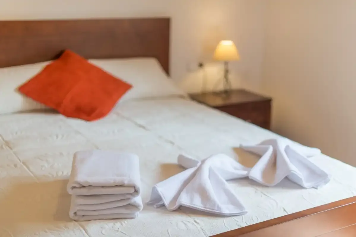 A bedroom with a neatly made bed and folded towels at the foot.