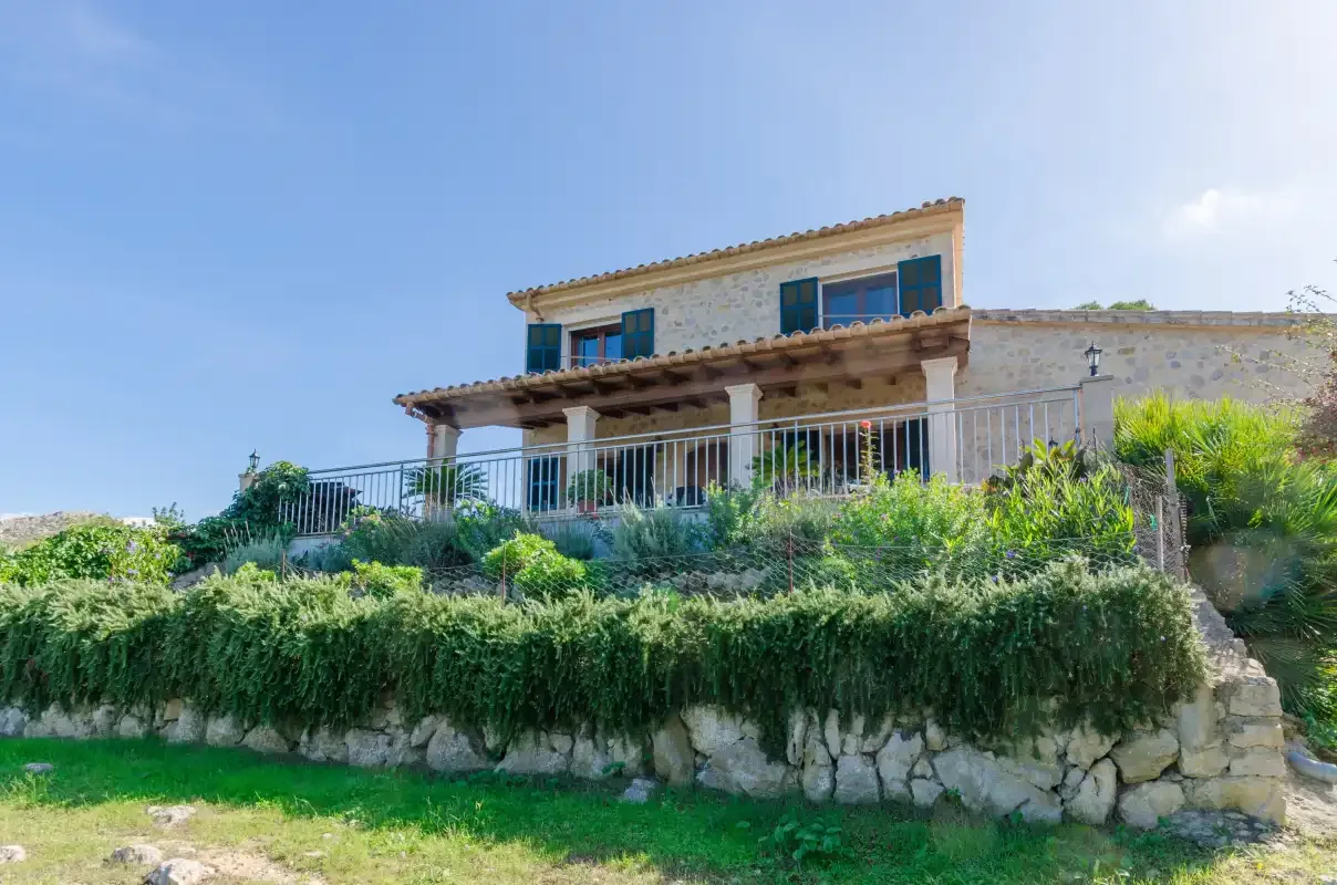 A two-story house with a covered terrace stands above a stone retaining wall.