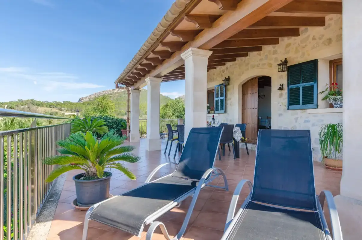 A covered patio with lounge seating overlooks greenery and the surrounding landscape.