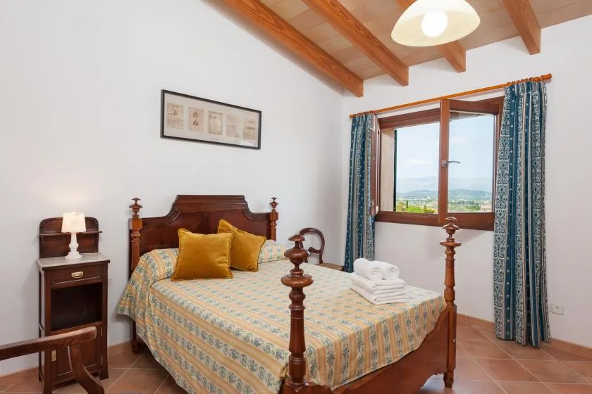 A bedroom with a wooden bed, patterned bedding, and a curtained window.