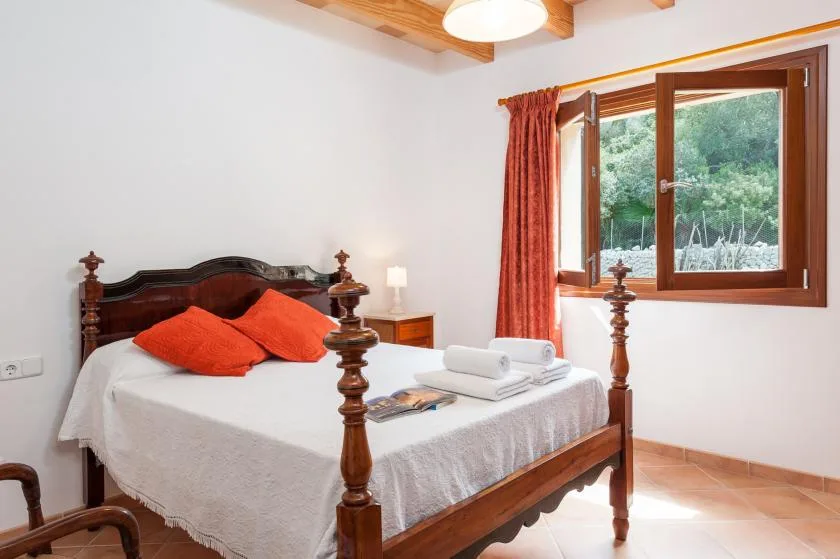 A bedroom with a wooden bed, white bedding, and a window overlooking greenery.