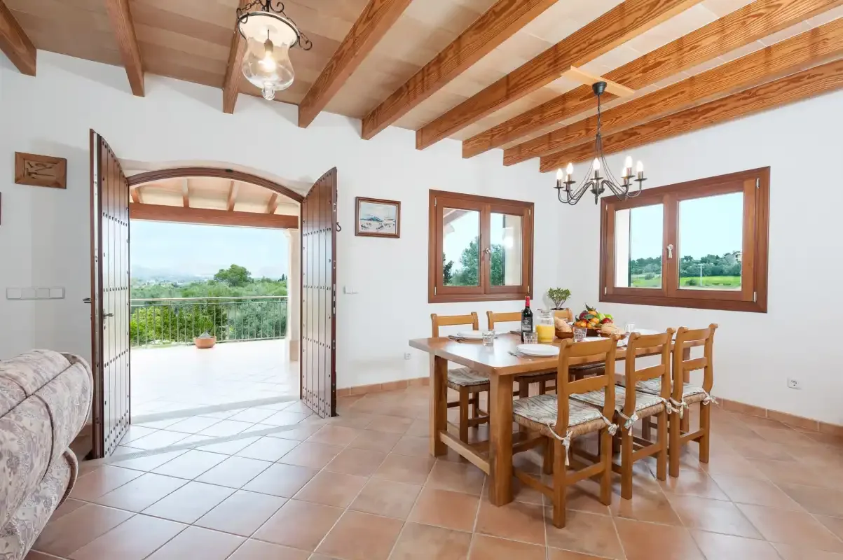 A dining area with a wooden table and chairs beside an open doorway to a terrace.
