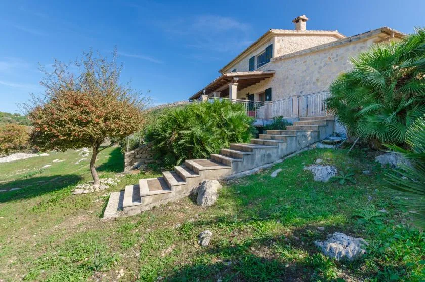 A stone house stands above outdoor steps amid trees and greenery.